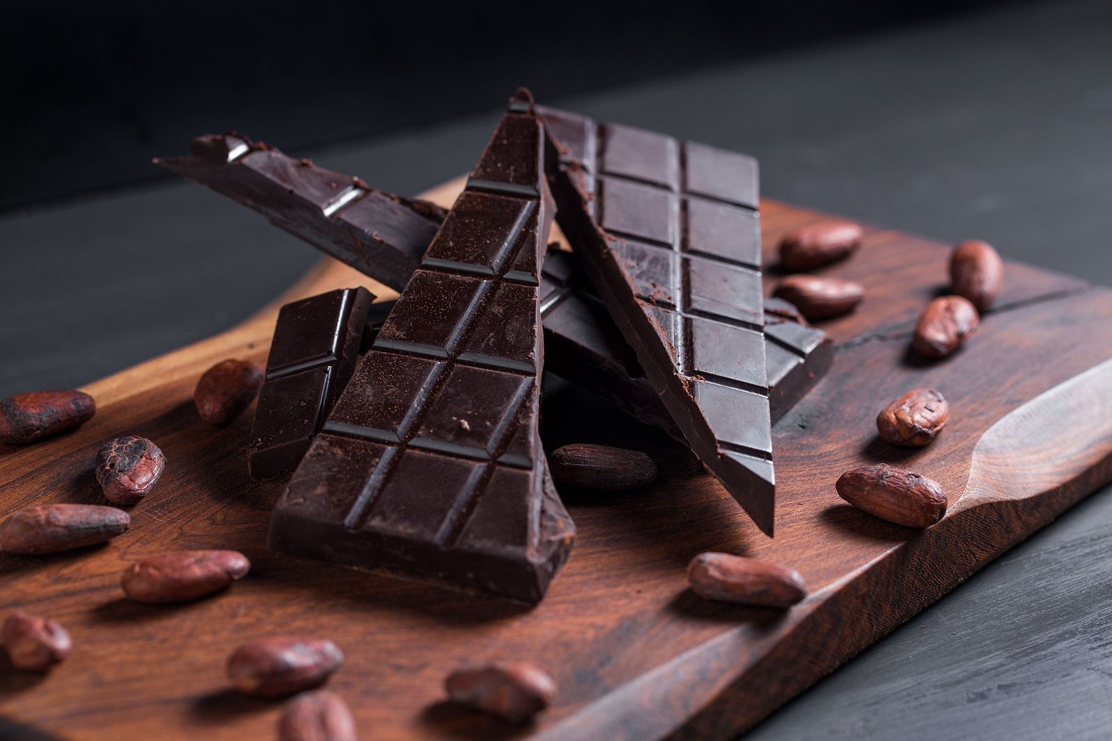 Chocolate amargo partido sobre tabla de madera con habas de cacao